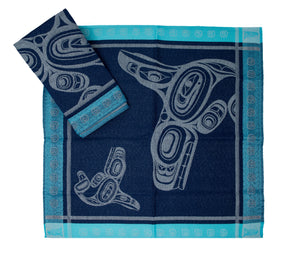 A dark blue woven cloth napkin decorated with a grey Orca design and a turquoise dotted border.