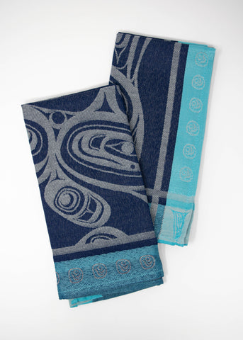 A dark blue woven cloth napkin decorated with a grey Orca design and a turquoise dotted border. The napkins are folded vertically and slightly overlapping.