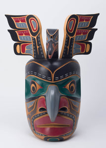 Yellow cedar mask with a hooked nose painted in black, green, grey, and red, with a bird and protruding wings coming out of the top of the head.
