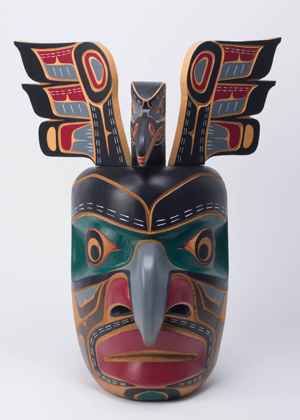 Yellow cedar mask with a hooked nose painted in black, green, grey, and red, with a bird and protruding wings coming out of the top of the head.