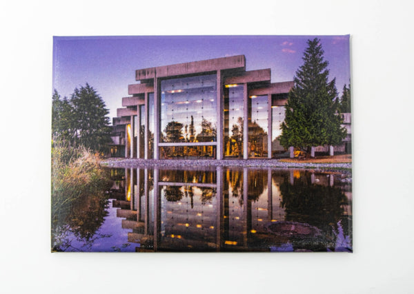 A rectangular magnet depicting a photo of the building of the Museum of Anthropology in the evening. The building is reflected in a pool, and the background contains trees and a purple sky.