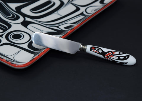 A spreader knife with a white handle, printed with a red and black eagle design.