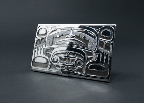 A shiny silver business card holder with a symmetrical formline bear etched onto the front.