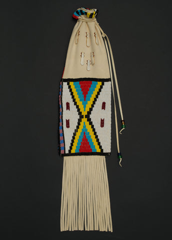 A long, flat drawstring bag made from cream hide with long fringes on the bottom. A large rectangular chevon design on the front is beaded with white, black, yellow, turquoise, and red beads.