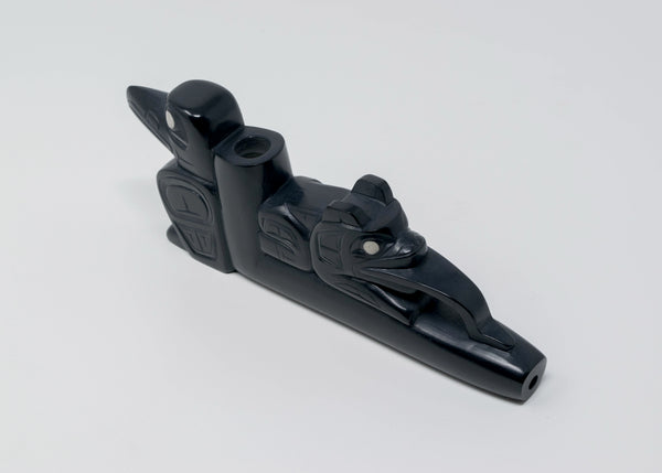 Black carved stone pipe with a frog figure facing the lip, and a raven figure on the end of the bowl.