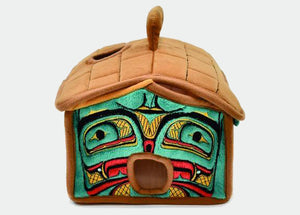A plush house with a brown roof and handle, and a green, white, and red embroidered front.